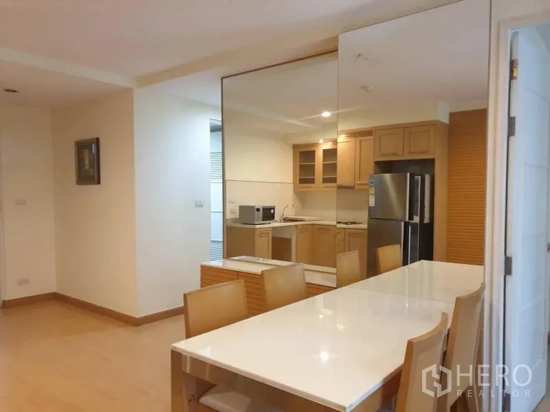Condominium for rent in Watthana, Bangkok - Open-plan dining area with long table and mirrored wall beside the fitted kitchen.
