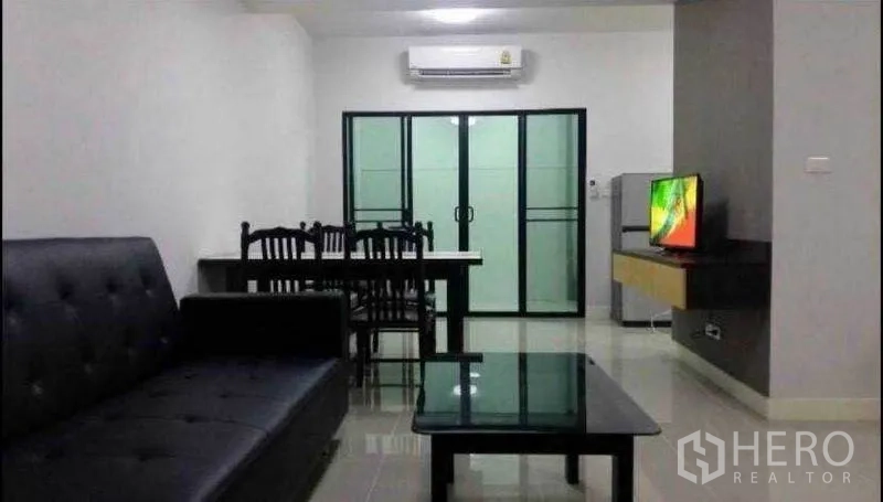 Townhouse for rent in Suan Luang, Bangkok - Living room with black sofa, glass coffee table, dining table, air conditioner and sliding glass doors.