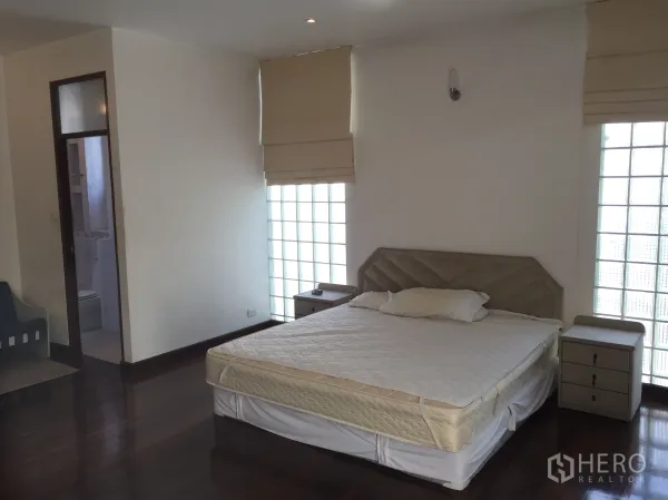 公寓 出租在Watthana, Bangkok - 明亮卧室，配特大床、玻璃砖窗、床头柜及通往套卫的门。