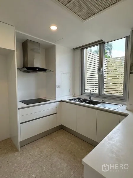 Townhouse for sale in Yan Nawa, Bangkok - Compact white L-shaped kitchen with window, induction hob and range hood.