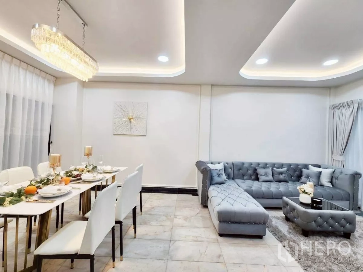 Townhouse for rent in Huai Khwang, Bangkok - Combined living and dining area with chandelier, upholstered sofa and glossy tile floor.