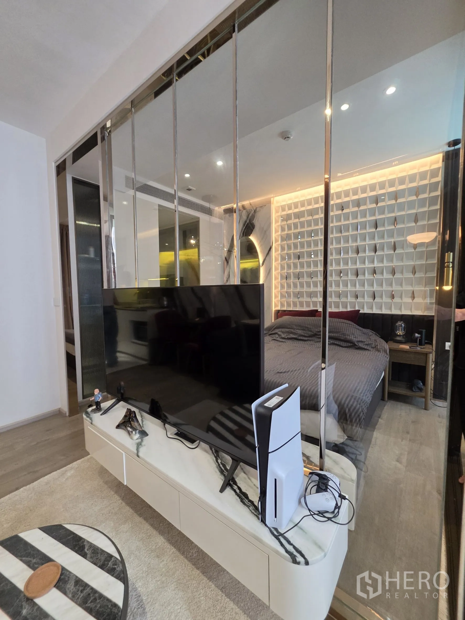 Condominium for rent in Khlong Toei, Bangkok - TV on a marble console set against a mirrored divider beside the bedroom.