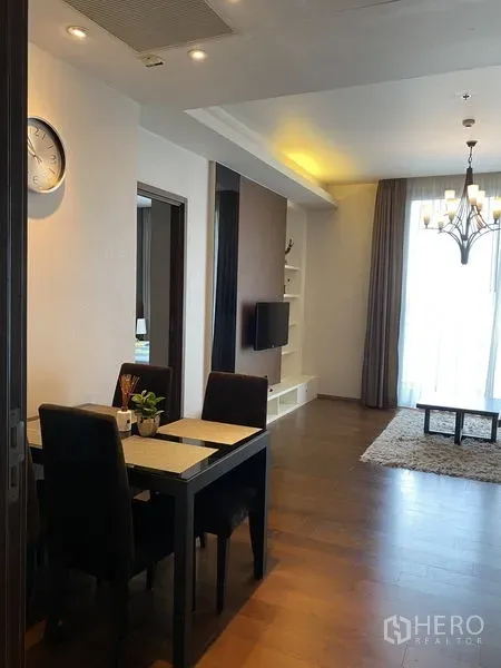 Condominium for rent in Watthana, Bangkok - Dining nook and hallway opening to a bright living room with TV wall, chandelier and tall curtains.