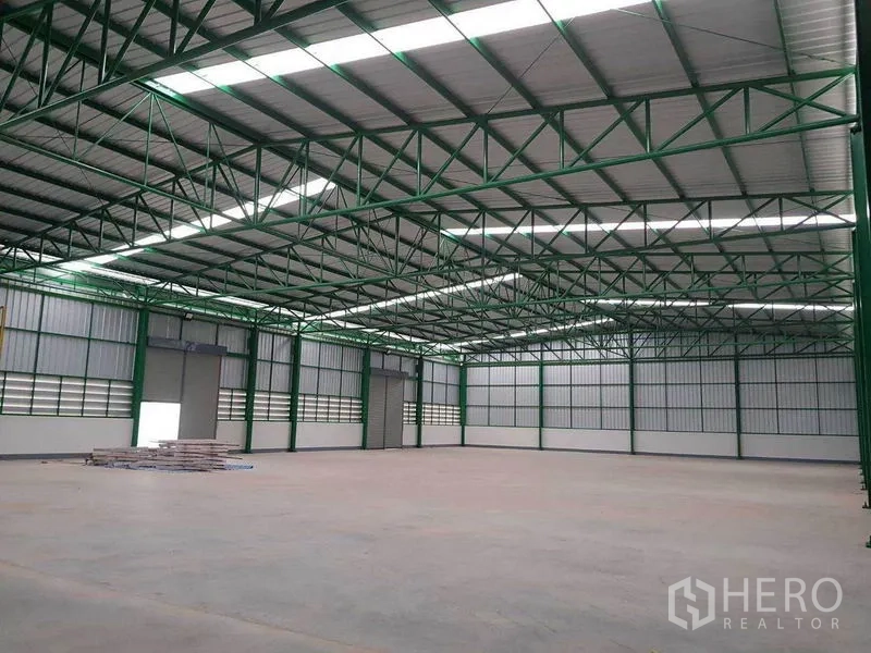 Warehouse for rent in Prawet, Bangkok - Clear-span warehouse interior with high green steel trusses, skylight panels and smooth concrete floor.
