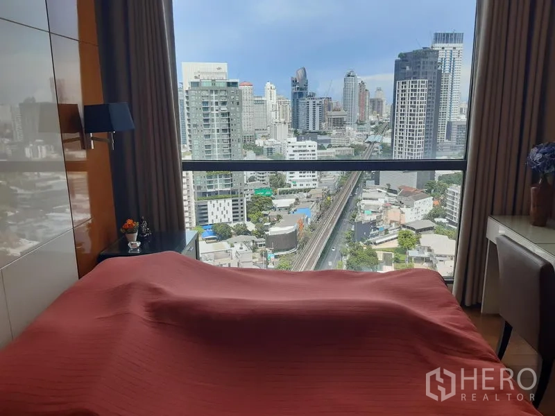 Condominium for rent in Khlong Toei, Bangkok - Bedroom with a large picture window overlooking the city skyline and BTS Skytrain tracks.