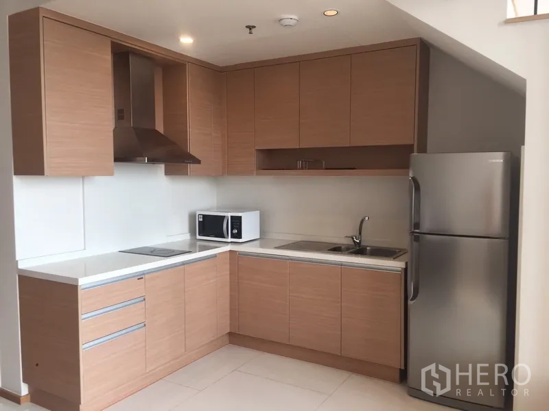 公寓 出租在Khlong Toei, Bangkok - L形现代厨房，浅木柜、抽油烟机、灶台、水槽、微波炉与冰箱。