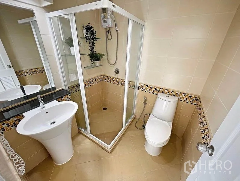 Condominium for rent in Khlong Toei, Bangkok - Bathroom with glass-enclosed shower, pedestal sink and beige tiles.