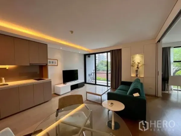 คอนโด ให้เช่าในWatthana, Bangkok - ห้องนั่งเล่นสว่าง พร้อมครัวเปิด โซฟาสีเขียว ทีวี และระเบียงวิวต้นไม้