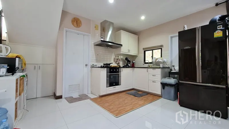 Detached House for sale in Samut Prakan - Modern white kitchen with built-in oven, cooktop and stainless hood.