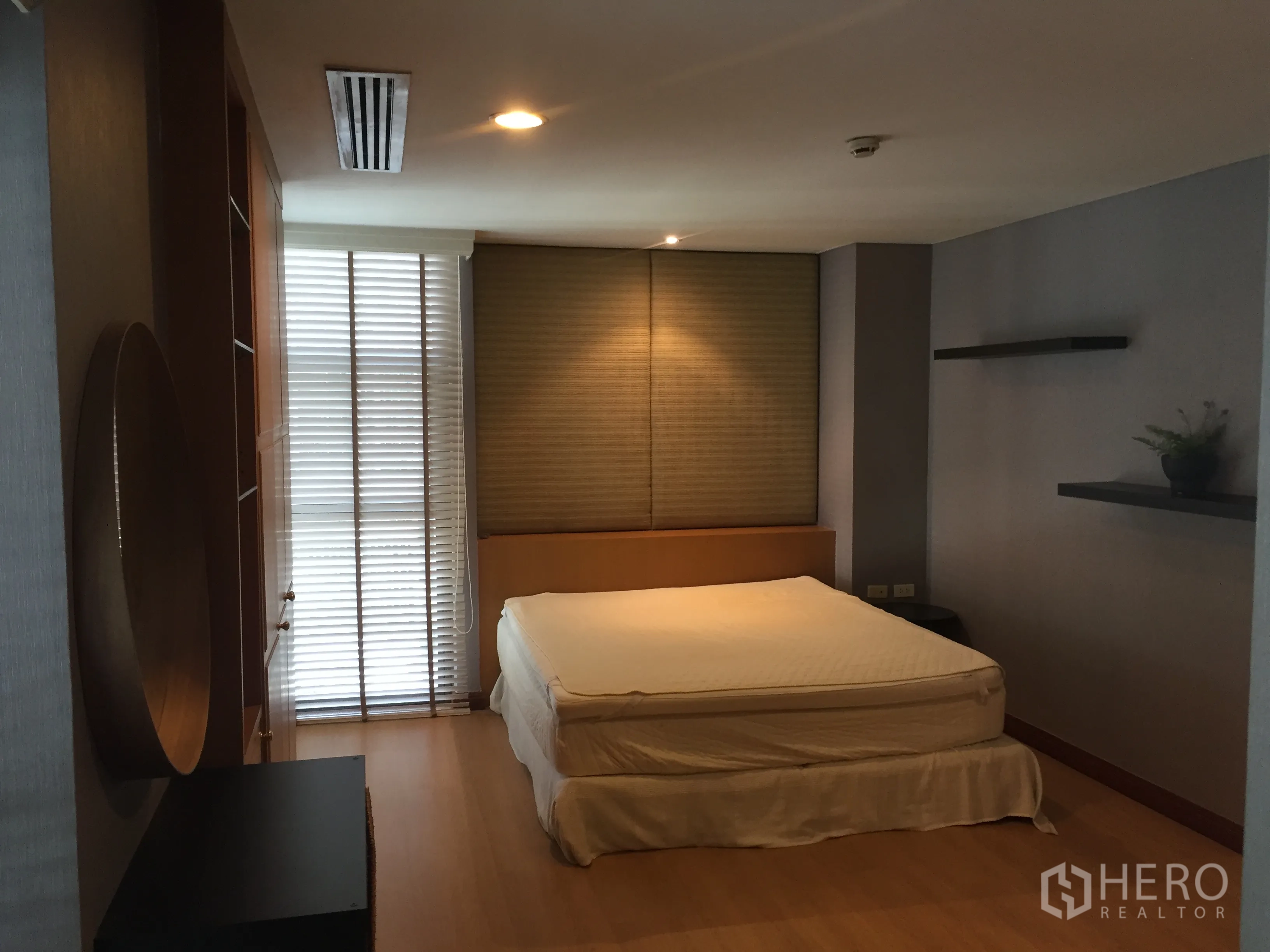 Condominium for rent in Pathum Wan, Bangkok - Spacious master bedroom with king bed, shelves, large window with blinds, and wood flooring.