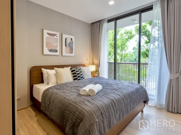 Condominium for rent or sale in Watthana, Bangkok - Primary bedroom with king bed and floor-to-ceiling glass to a green balcony view.