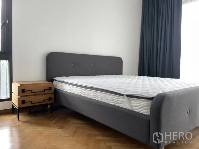 独栋房屋 for rent in Watthana, Bangkok - 明亮卧室，灰色软包床、木质床头柜与人字拼木地板。
