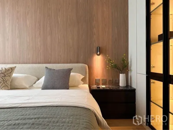 Condominium for rent in Pathum Wan, Bangkok - Warm bedroom with wood accent wall, sconce-lit nightstand and a backlit glass wardrobe in a Chitlom condo.