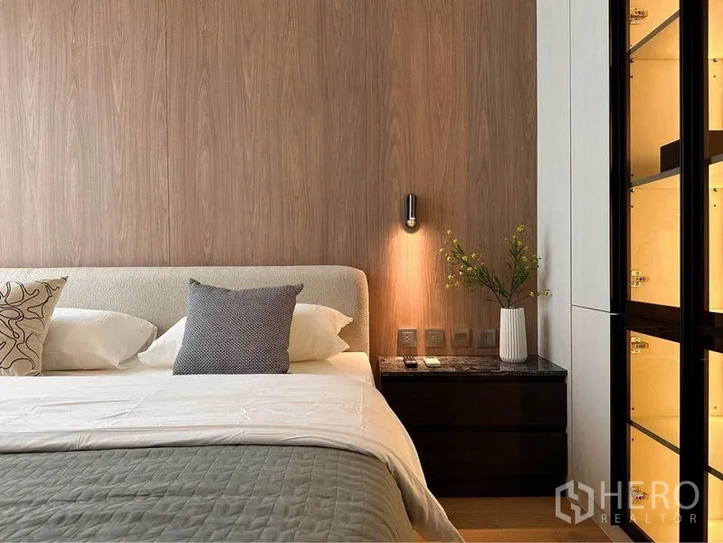 Condominium for rent in Pathum Wan, Bangkok - Warm bedroom with wood accent wall, sconce-lit nightstand and a backlit glass wardrobe in a Chitlom condo.