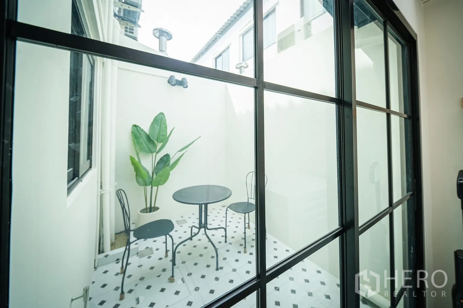 Townhouse for rent in Bang Phli, Samut Prakan - View through black-framed sliding doors to a small tiled courtyard with bistro table and chairs.