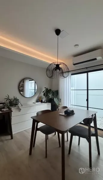 Townhouse for rent in Bang Phli, Samut Prakan - Cozy dining corner with round mirror, white sideboard, air conditioner and sliding glass door to patio.