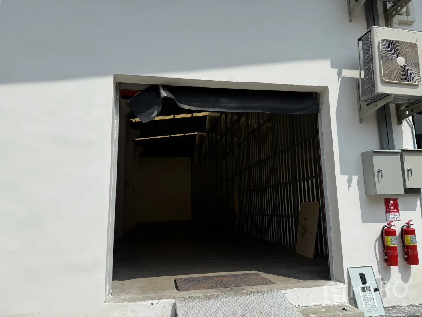 Warehouse for rent in Suan Luang, Bangkok - Warehouse entrance with wide opening, loading ramp, control boxes and fire extinguishers on the exterior wall.