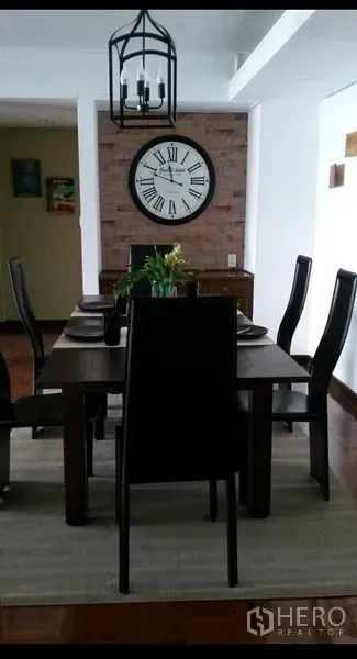 Condominium for rent in Khlong Toei, Bangkok - Dining area with wooden table and six chairs, lantern-style chandelier and large wall clock on brick feature wall.