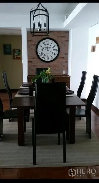 Condominium for rent in Khlong Toei, Bangkok - Dining area with wooden table and six chairs, lantern-style chandelier and large wall clock on brick feature wall.