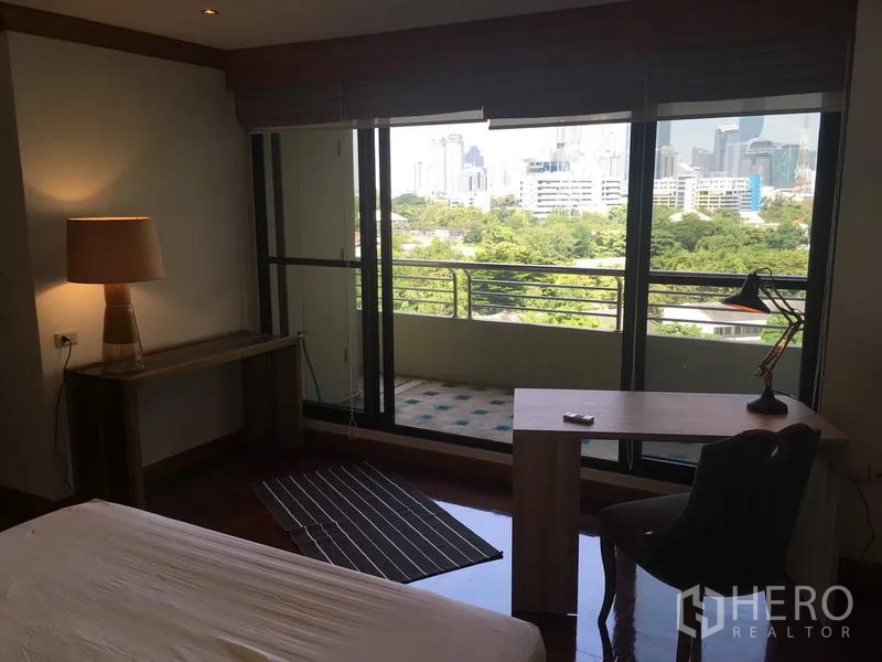 Condominium for rent in Sathon, Bangkok - Bedroom with floor-to-ceiling windows and balcony access showcasing a green city skyline view.