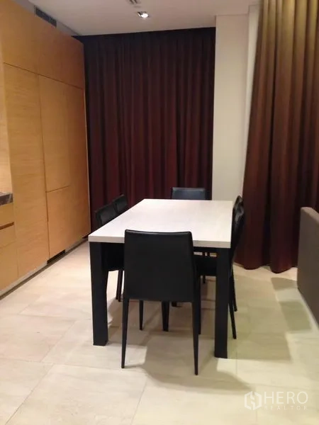 Condominium for sale in Bang Rak, Bangkok - Dining corner with four black chairs and a rectangular table beside tall curtains.