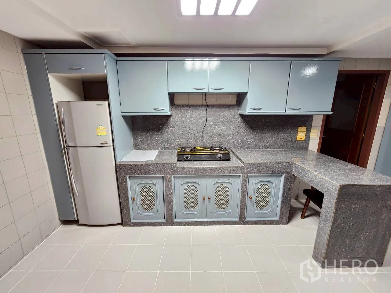 Condominium for rent in Khlong Toei, Bangkok - Kitchen worktop with gas cooktop, overhead storage and grey stone surfaces.