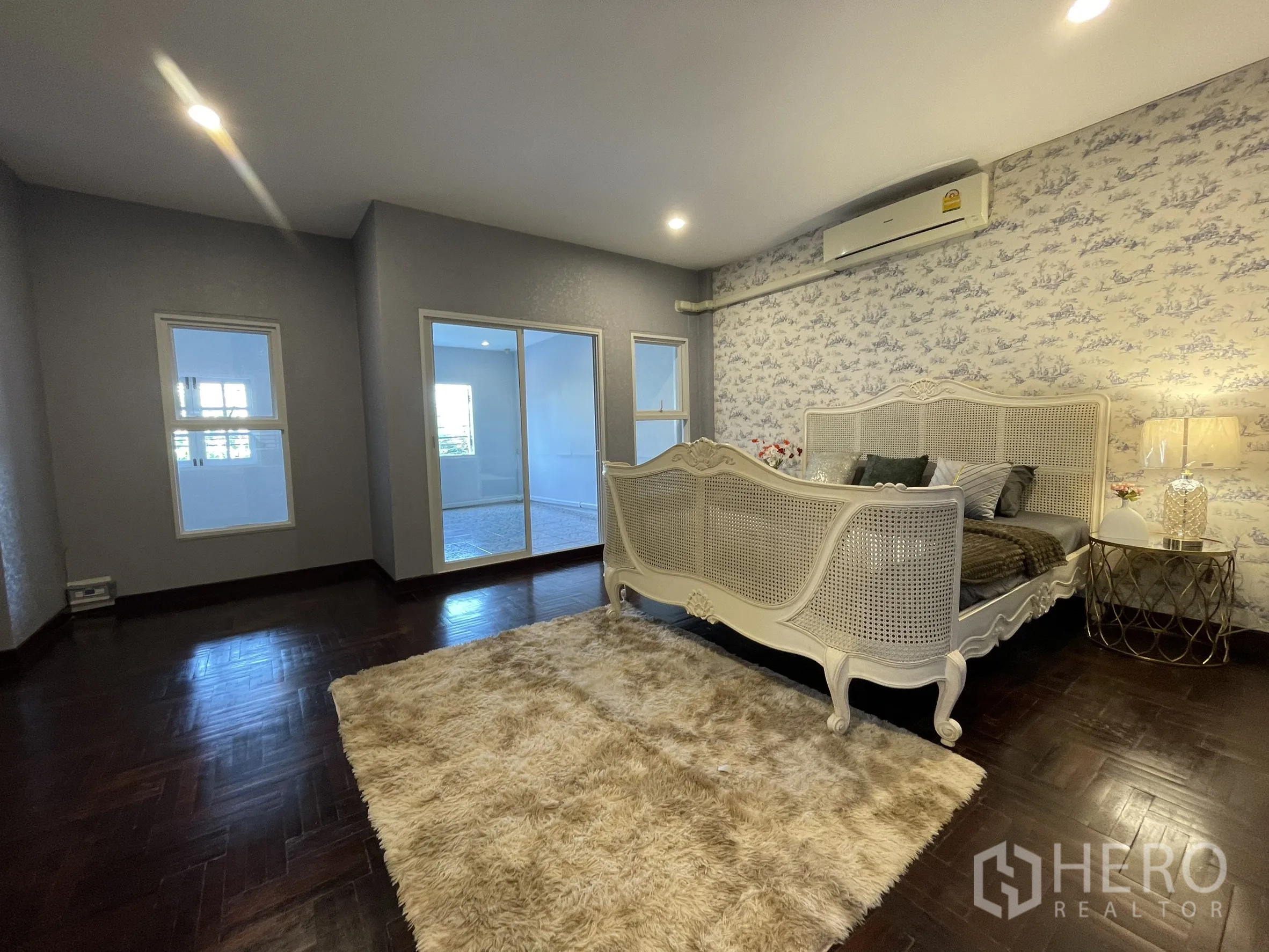 店屋 for rent in Bang Kapi, Bangkok - 宽敞卧室配复古藤编床、深色人字拼地板与通往采光房的推拉玻璃门。