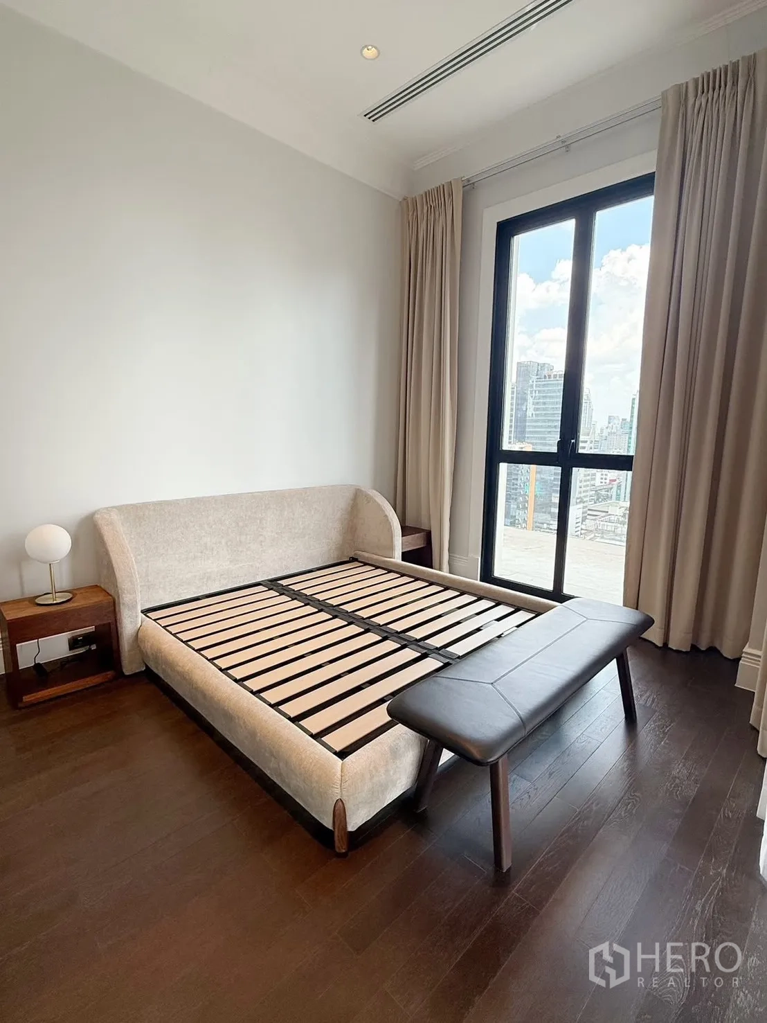 คอนโด for rent or sale in Pathum Wan, Bangkok - ห้องนอนสว่างเตียงบุผ้านุ่มพร้อมม้านั่ง ปูพื้นไม้สีเข้มและหน้าต่างบานใหญ่เห็นวิวเมือง