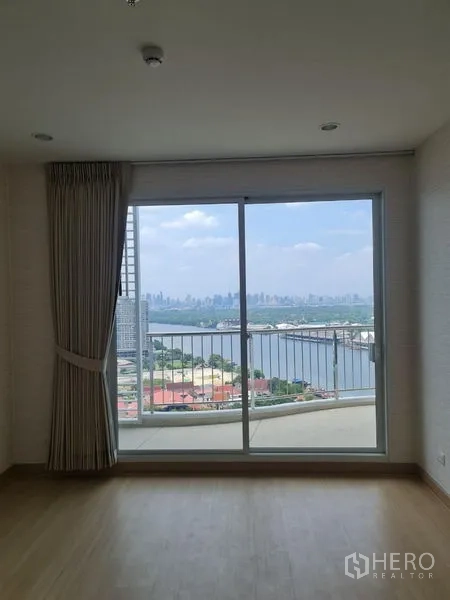 公寓 出售在Yan Nawa, Bangkok - 明亮房间，推拉落地门通向阳台，远眺江景与城市天际线。