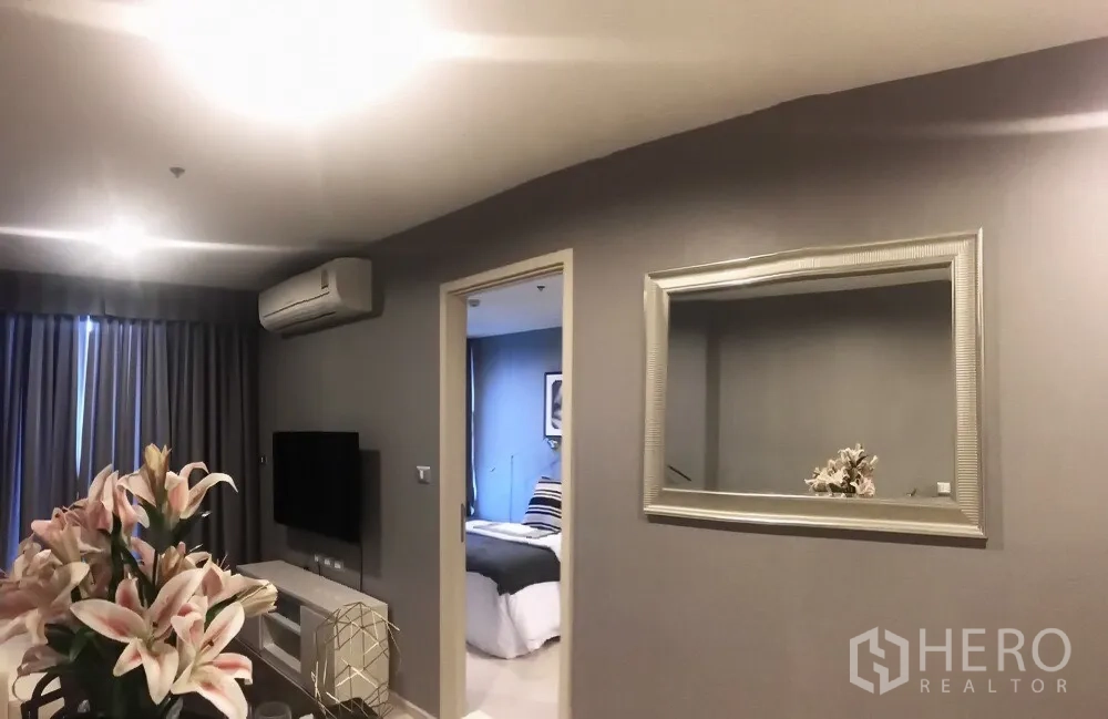 Condominium for sale in Khlong Toei, Bangkok - Living area view toward the bedroom with a large wall mirror, TV and draped windows.