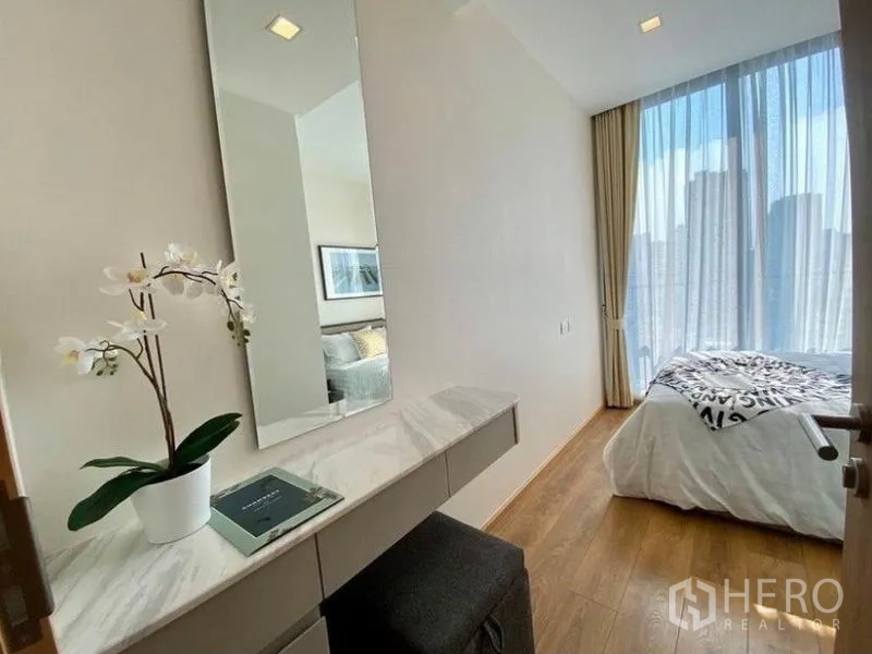 公寓 出租在Watthana, Bangkok - 走廊化妆台与兰花，通往明亮卧室和城市景观。