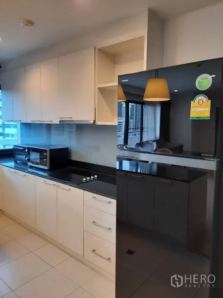 Condominium for rent in Watthana, Bangkok - Close-up of fitted kitchen cabinetry with glossy black refrigerator and built-in appliances.