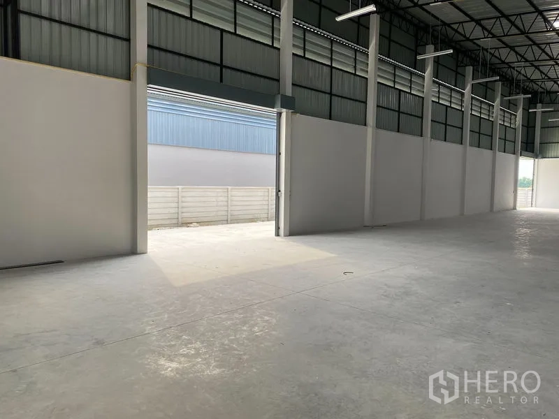 Warehouse for rent or sale in Bang Len, Nakhon Pathom - Large roller shutter opening from the warehouse to a secure outdoor yard with boundary wall.