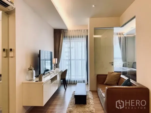 คอนโด ให้เช่าในWatthana, Bangkok - ห้องนั่งเล่นสว่างพร้อมโซฟาหนัง ตู้ทีวี และกระจกเต็มบานเปิดสู่ระเบียง กั้นห้องนอนด้วยกระจก