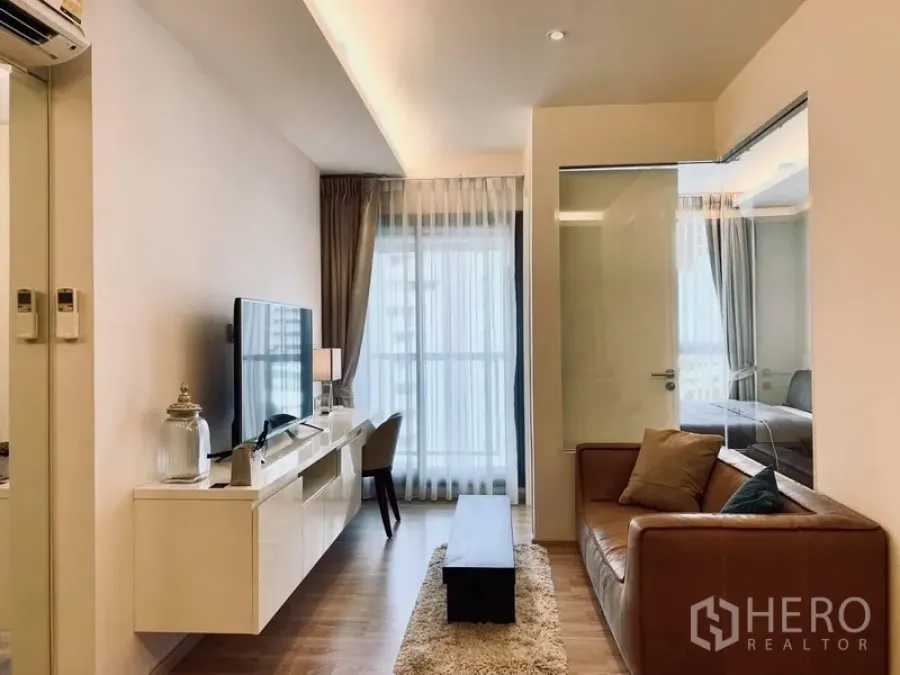 公寓 出租在Watthana, Bangkok - 明亮客厅，皮沙发、电视柜与落地窗，玻璃隔断通往卧室。
