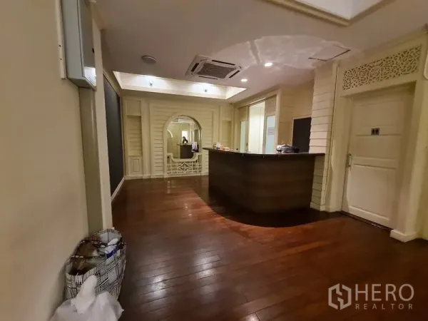 Shophouse for rent in Khlong Toei, Bangkok - Reception area with curved counter, dark hardwood floors, an arched feature wall and recessed lighting.