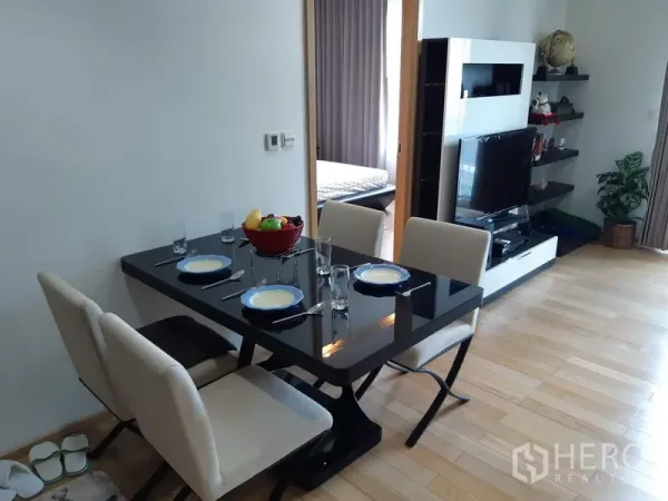 Condominium for rent in Khlong Toei, Bangkok - Dining area with a black glass table set for four beside the open-plan living room and bedroom doorway.