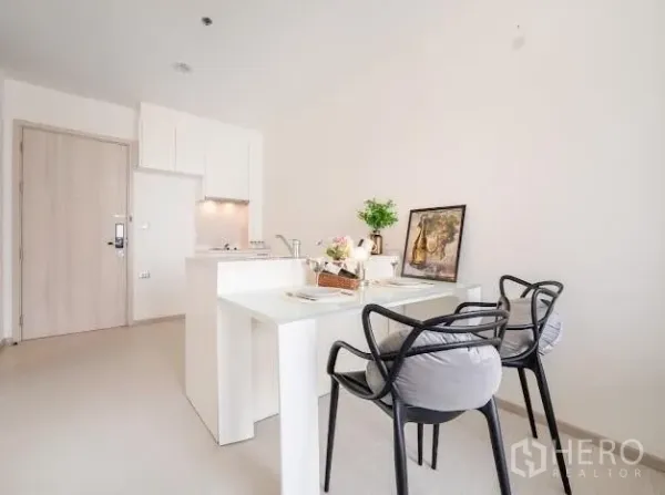 Condominium for sale in Khlong Toei, Bangkok - Dining nook with breakfast bar and two black chairs beside the compact kitchen.