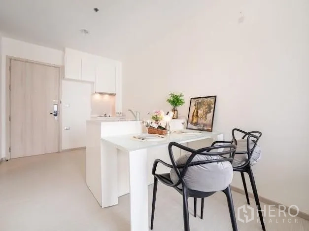 Condominium for sale in Khlong Toei, Bangkok - Dining nook with breakfast bar and two black chairs beside the compact kitchen.