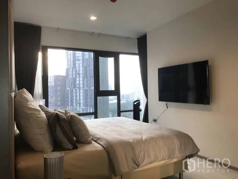 Condominium for rent or sale in Khlong Toei, Bangkok - Corner bedroom with panoramic windows and mounted TV overlooking the city.