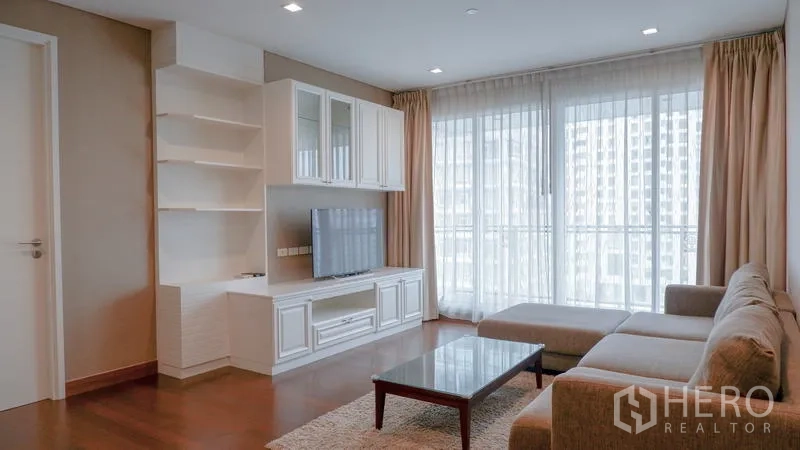 Condominium for rent in Watthana, Bangkok - Living area with TV cabinet and floor-to-ceiling windows opening to the balcony.