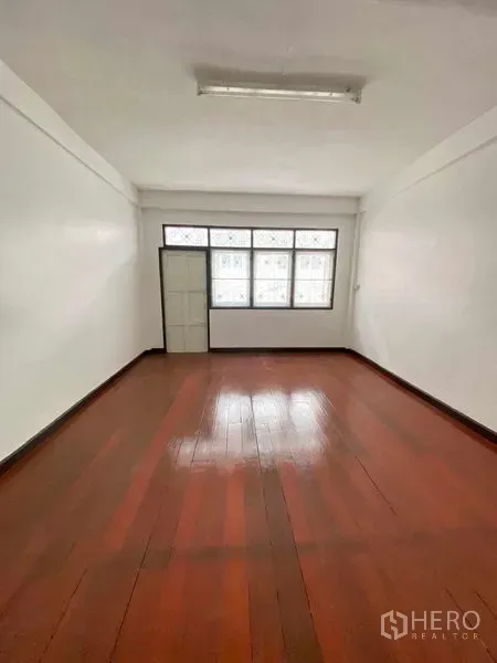 Shophouse for sale in Phra Khanong, Bangkok - Bright upper room with wooden floor, frosted windows and a single door in the shophouse.