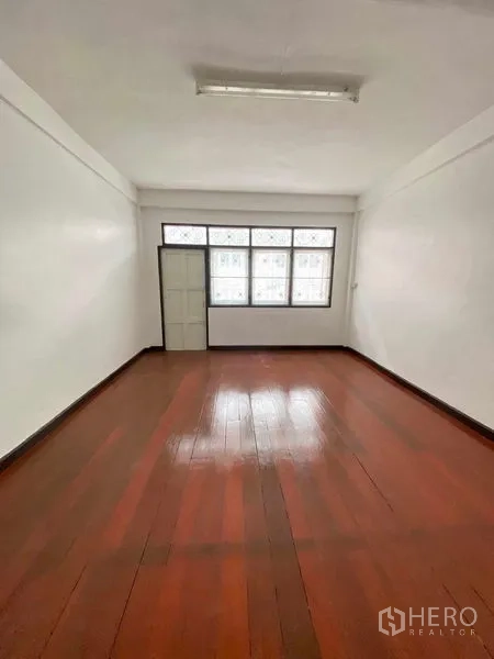Shophouse for sale in Phra Khanong, Bangkok - Bright upper room with wooden floor, frosted windows and a single door in the shophouse.