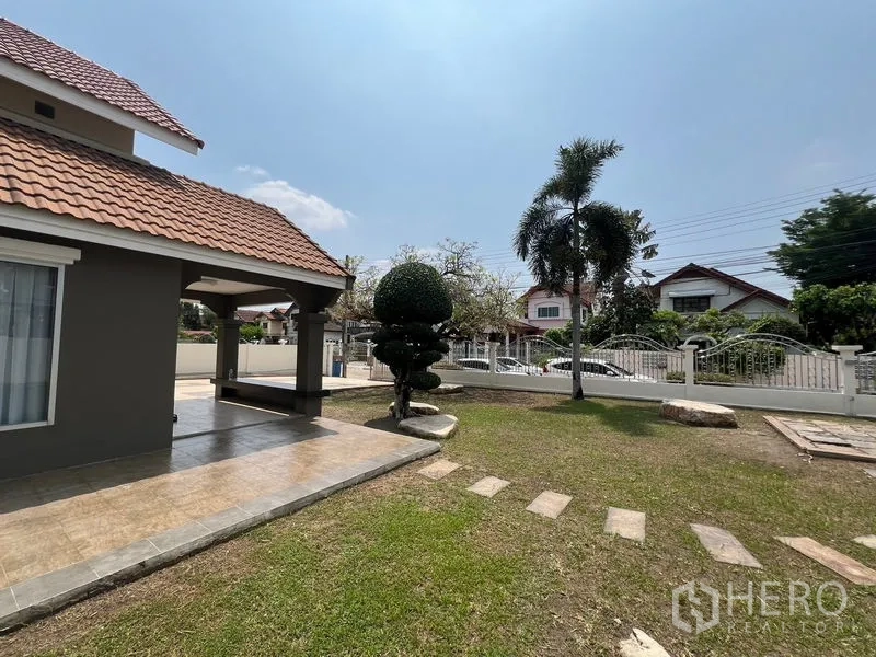 独立式住宅 出售在Mueang Pathum Thani, Pathum Thani - 有顶露台旁的修剪树、卵石小径与棕榈。