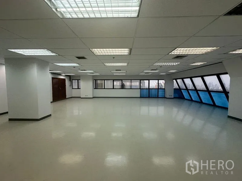 办公空间 出租在Phaya Thai, Bangkok - 明亮开放式办公室，悬挂式照明、多根立柱与两侧蓝色外窗。