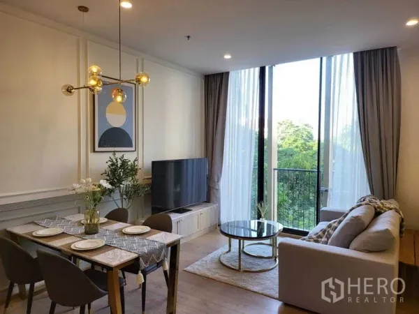 Condominium for rent in Watthana, Bangkok - Living room with TV console, sofa and glass doors opening to a balcony overlooking green treetops.