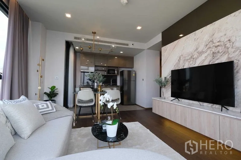 Condominium for rent in Khlong Toei, Bangkok - Open-plan living room with marble TV wall, large sofa, and adjoining kitchen.