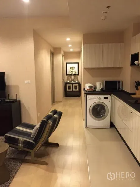 Condominium for rent in Watthana, Bangkok - Compact kitchenette with washer, microwave and countertop, plus hallway leading to bedrooms in a modern condo.