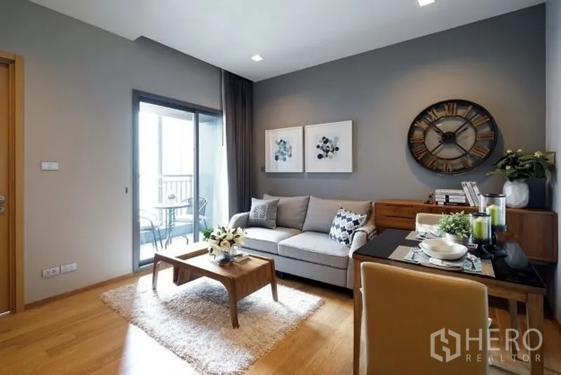 公寓 出租在Watthana, Bangkok - 明亮客厅，灰色强调墙、沙发与用餐角，推门连接小阳台的曼谷现代公寓。