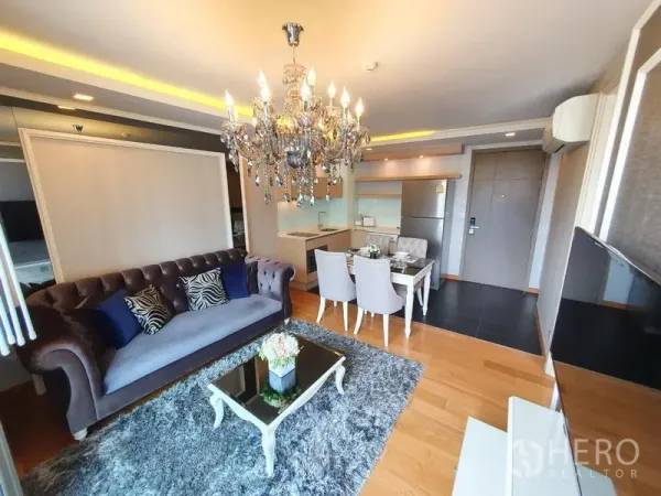 Condominium for rent in Watthana, Bangkok - Living area with velvet sofa, glass coffee table and chandelier facing the kitchenette in a modern condo.